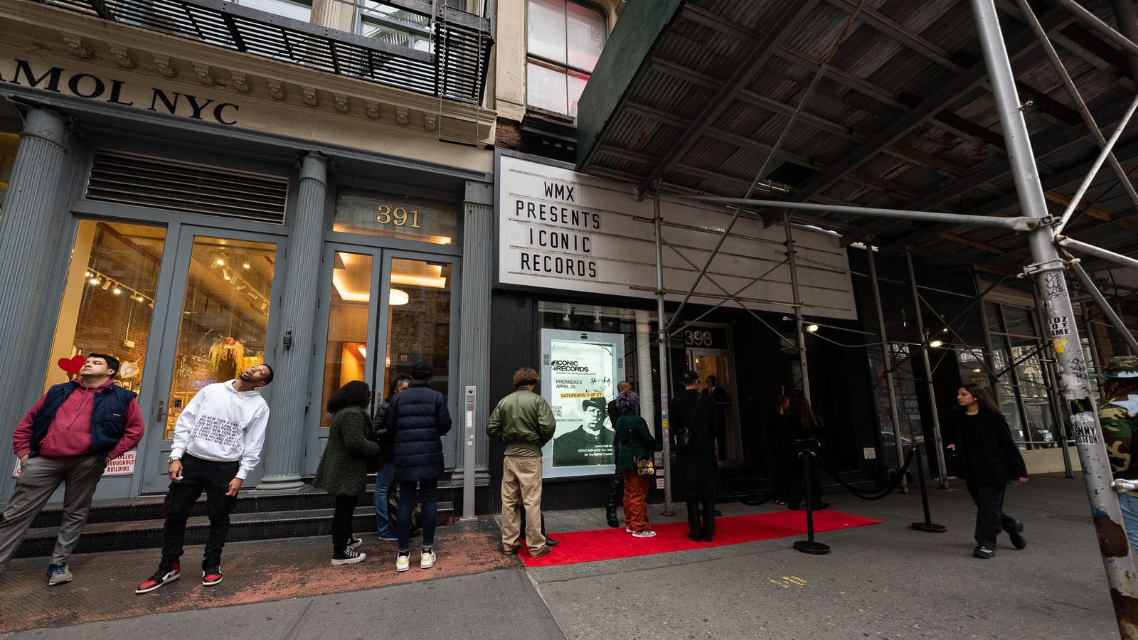 Guests queue on the sidewalk beside a red carpet under a WMX Presents marquee and scaffolding