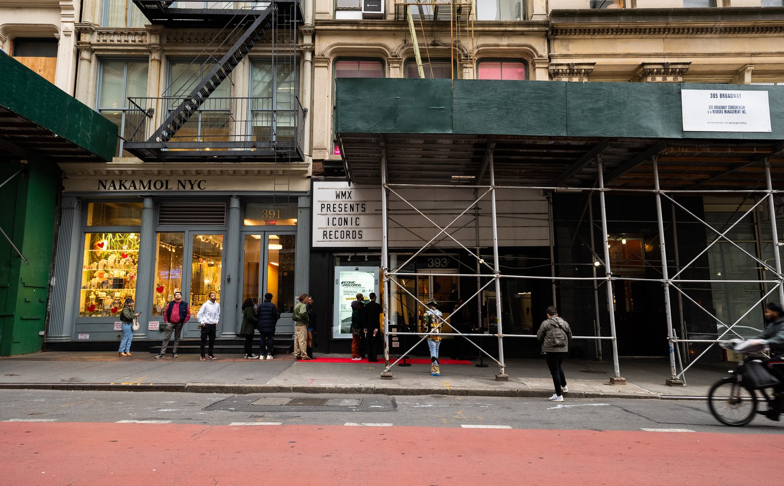 Wide street view of a WMX Presents marquee, green scaffolding and a cyclist in the red bike lane