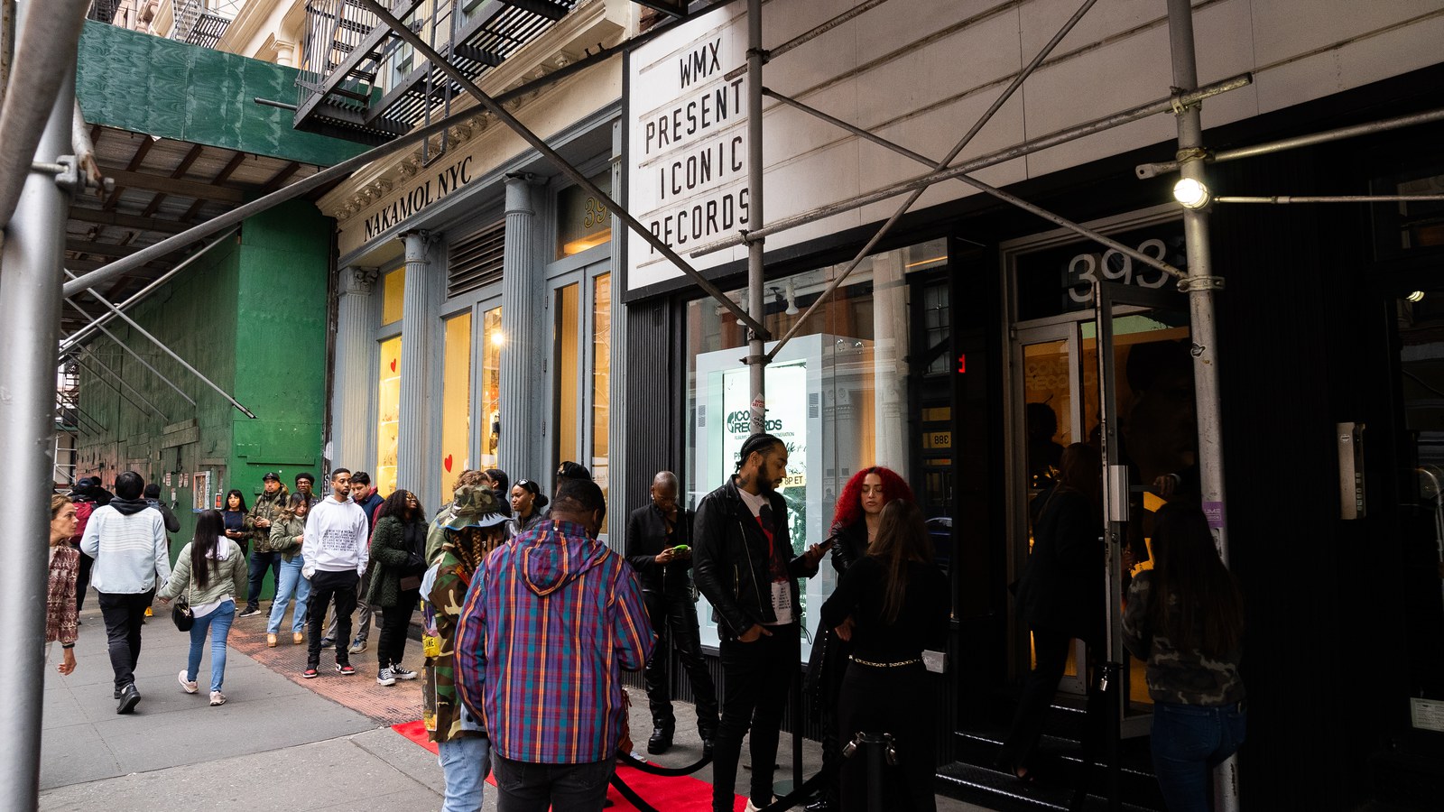 Guests arrive at a red carpet entrance beneath scaffolding as passersby walk along the sidewalk