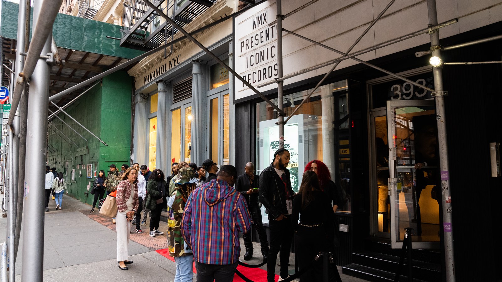Guests in colourful jackets gather at a red carpet entrance under scaffolding and a WMX Presents marquee
