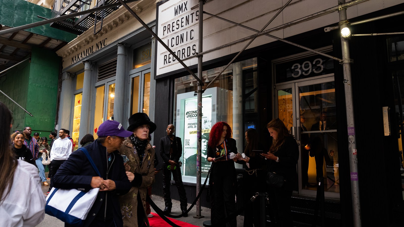 Woman in a purple cap with a white tote arrives at a red carpet entrance under a WMX Presents marquee