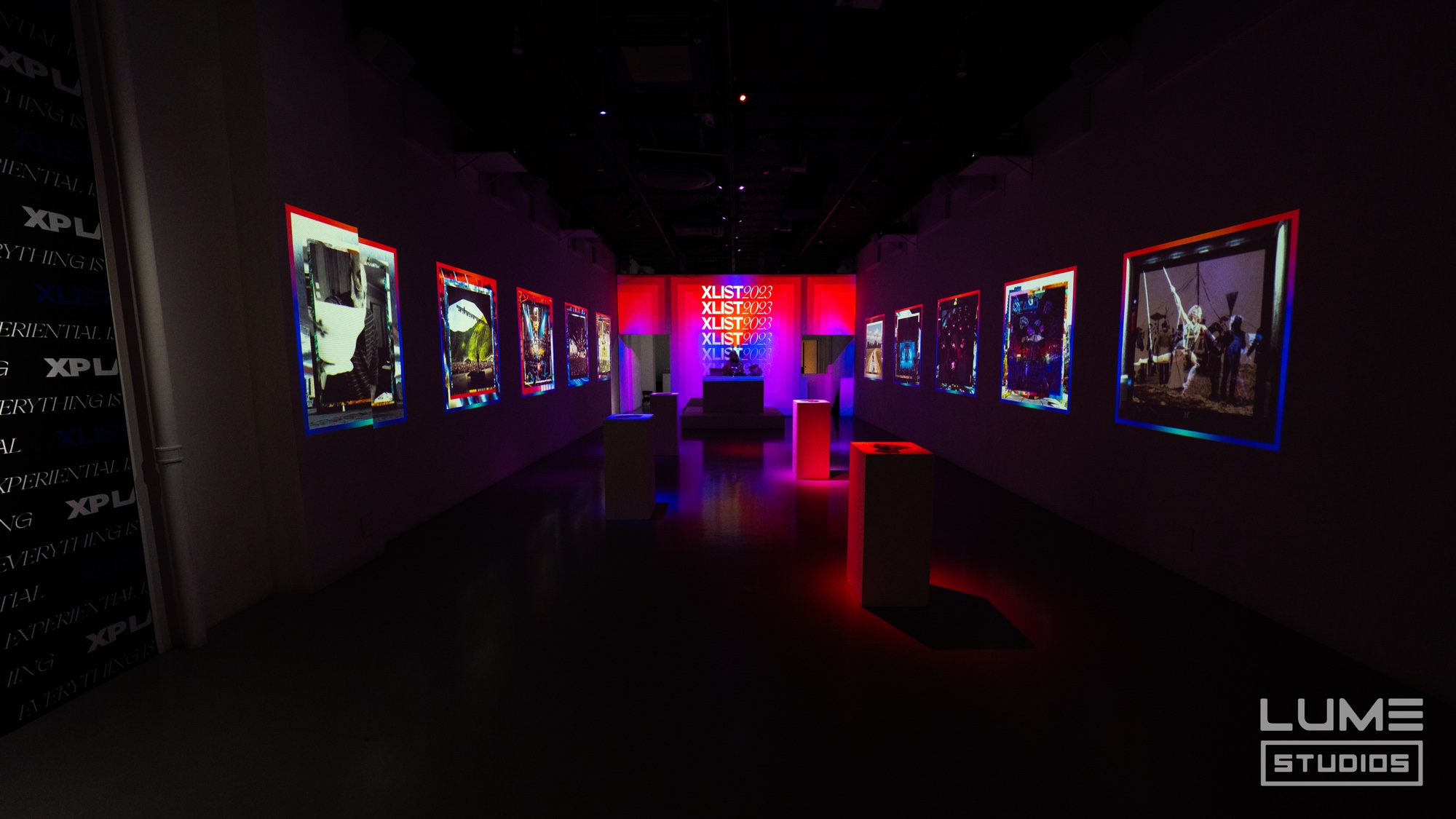 Dark gallery of backlit framed photographs and a glowing XLIST wall with red and blue lit plinths