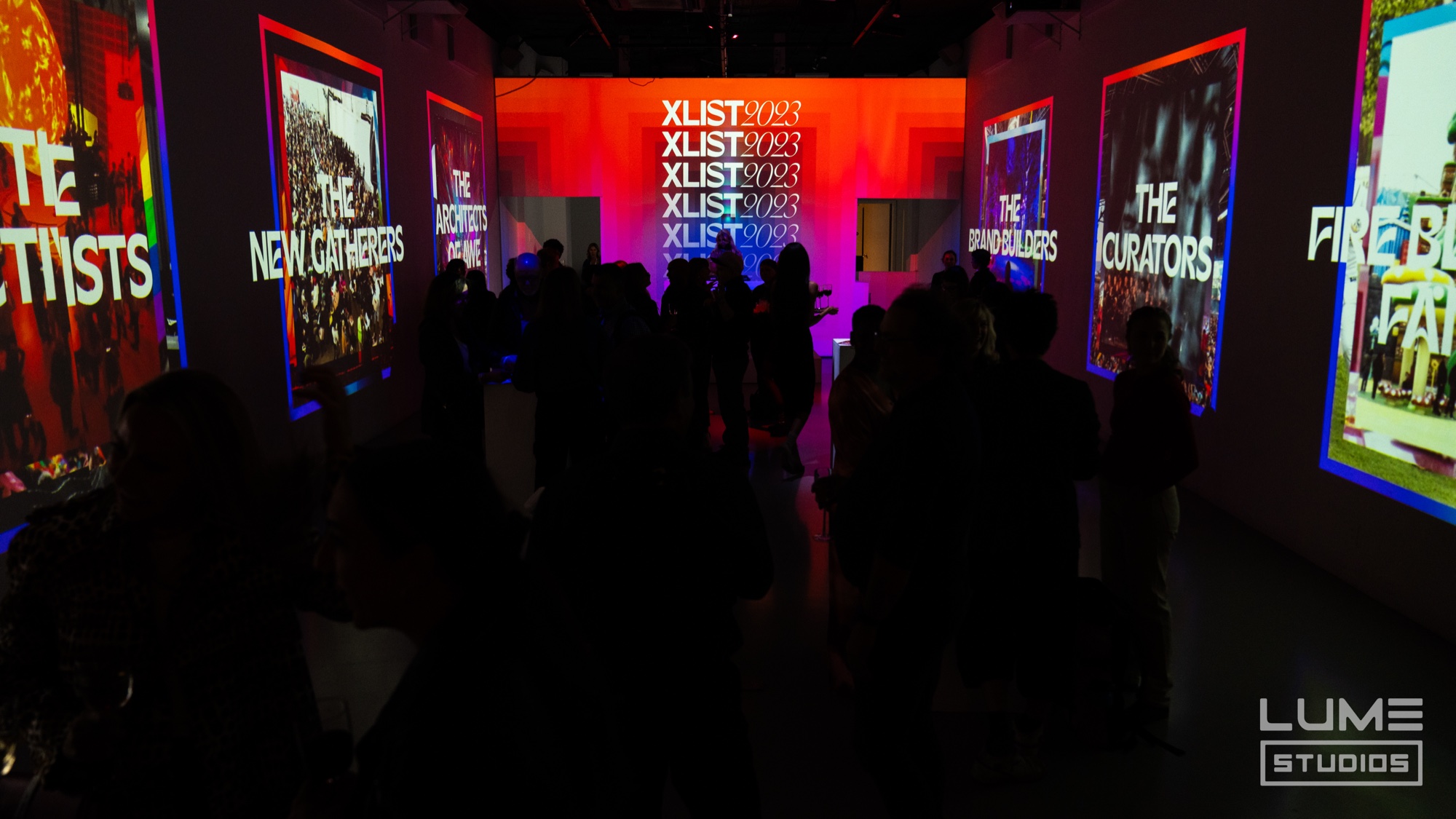 Dark hall lined with glowing framed panels, a red projection reading XList 2023 at the far end