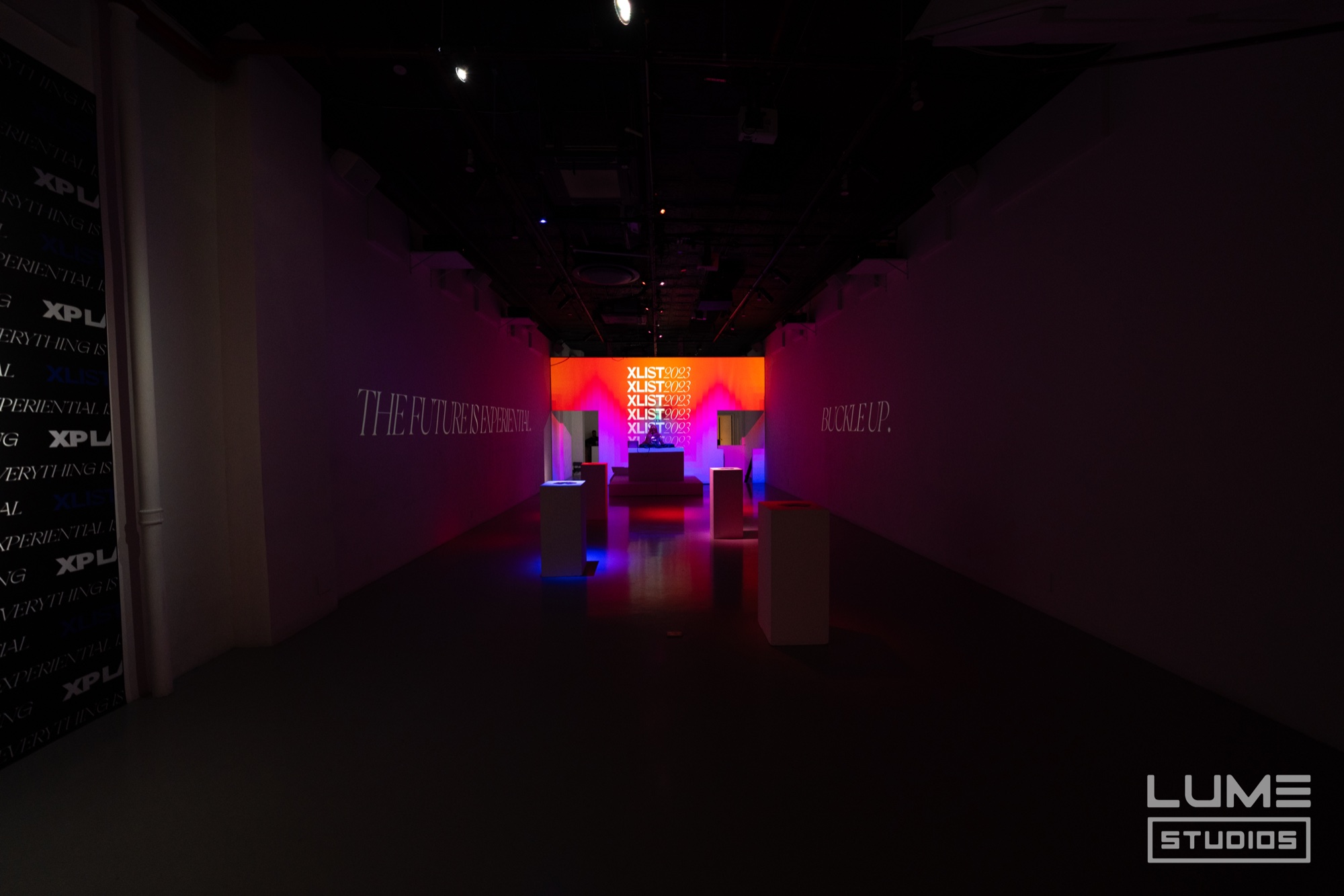 A dark corridor leads to a glowing orange and pink screen with white pedestals lit blue in the foreground