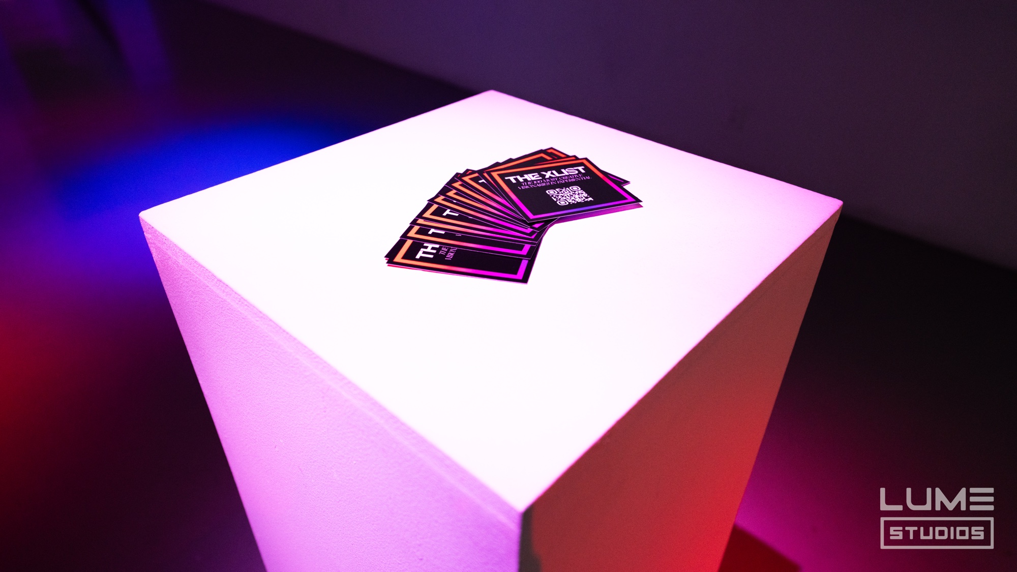 Fan of black The XLIST cards laid on a white plinth lit pink and blue